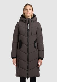 Gestepptes Anorak in Dunkelbraun mit passender Kapuze, schwarzen Akzenten, Reißverschluss und gestepptem Design mit Chevron-Mustern.
