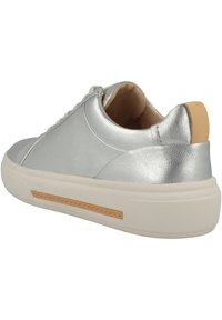 Sneaker in pelle argentata con una texture liscia, suola in gomma bianca e un accento sul tallone color beige. Presenta una chiusura con lacci e un interno imbottito.
