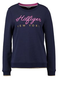 Sweatshirt marine en mélange de coton avec des manches longues, des poignets et un ourlet côtelés. Présente le logo "Hilfiger New York" rose et doré sur le devant.