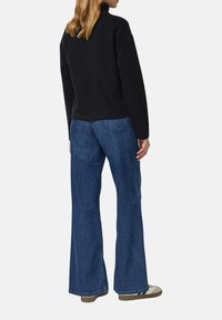 Schwarzer Fleece-Rollkragenpullover mit lockerem Schnitt, kombiniert mit weitem blauen Denim-Jeans. Helle Nähte an den Taschen und strukturierter Stoff.