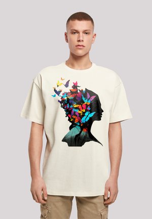 Cream oversized t-shirt featuring a black silhouette of a head adorned with colorful butterflies in pink, blue, yellow, and orange.
