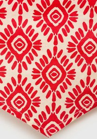 Röd och krämfärgad textil med ett diamantmönster och vågiga accenter. Texturen är slät, med djärva röda former som är omgivna av en ljusare röd.