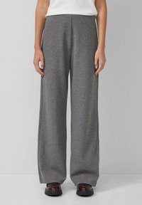 Graue weit geschnittene Hose aus weichem Stoff, mit lockerer Passform, hohem Bund und glatter Textur. Getragen mit dunklen Schuhen.
