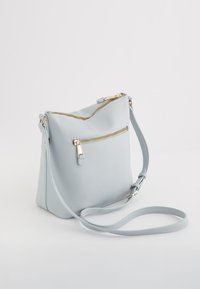 Geantă crossbody din piele albastră deschisă, cu accente aurii la fermoar, suprafață texturată și curea reglabilă; include un buzunar frontal cu fermoar.