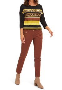 Haut à manches trois-quarts avec des rayures et motifs multicolores, associé à un pantalon ajusté couleur rouille avec des accents de boutons dorés.