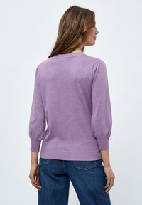 Lila gestrickter Pullover mit Ballonärmeln, gerippten Bündchen und Saum. Weicher Stoff und klassischer Rundhalsausschnitt, kombiniert mit dunkelblauen Jeans.
