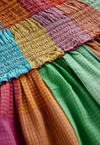 Close-up of colorful, pleated fabric with patchwork stitching in blue, yellow, red, green, and pink plaid patterns.