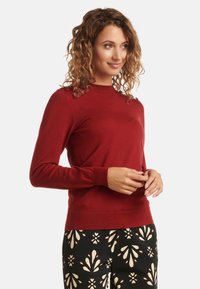 Red, knitted sweater with a crew neckline and long sleeves. Features a fitted design and ribbed cuffs, paired with patterned black pants.