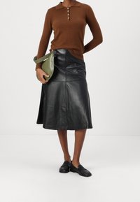 Maglione marrone a maniche lunghe con colletto e bottoni, abbinato a una gonna in pelle nera fino al ginocchio e una borsa verde, con mocassini neri.