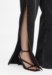 Sorte denim vide benbukser med sidesslisser, kombinert med sorte stroppestiletter med ankelrem og liten pendel detalj.
