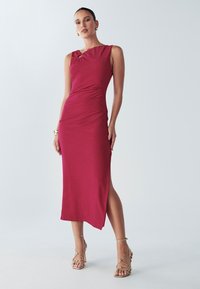 Sarkana, bezroku kleita ar rievotu detaļu uz pleca, pieguļošs siluets, vidēja garuma līdz teļiem, ar sānu šķēlumu, izgatavota no teksturēta auduma. Zelta krāsas sandales ar siksniņām.