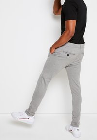 Šedé zúžené kalhoty vyrobené z látky s hladkým povrchem. Obsahují boční kapsy, zadní kapsu s knoflíkem a mají skloubený střih.