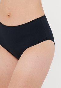 Woman wearing plain black high-waist cotton briefs, showing lower abdomen, hips, and upper thighs against a white background.