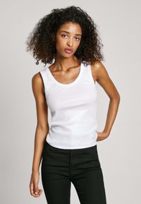 Top bianco senza maniche con scollo tondo, texture liscia e design aderente, abbinato a pantaloni neri. Look semplice e sobrio.
