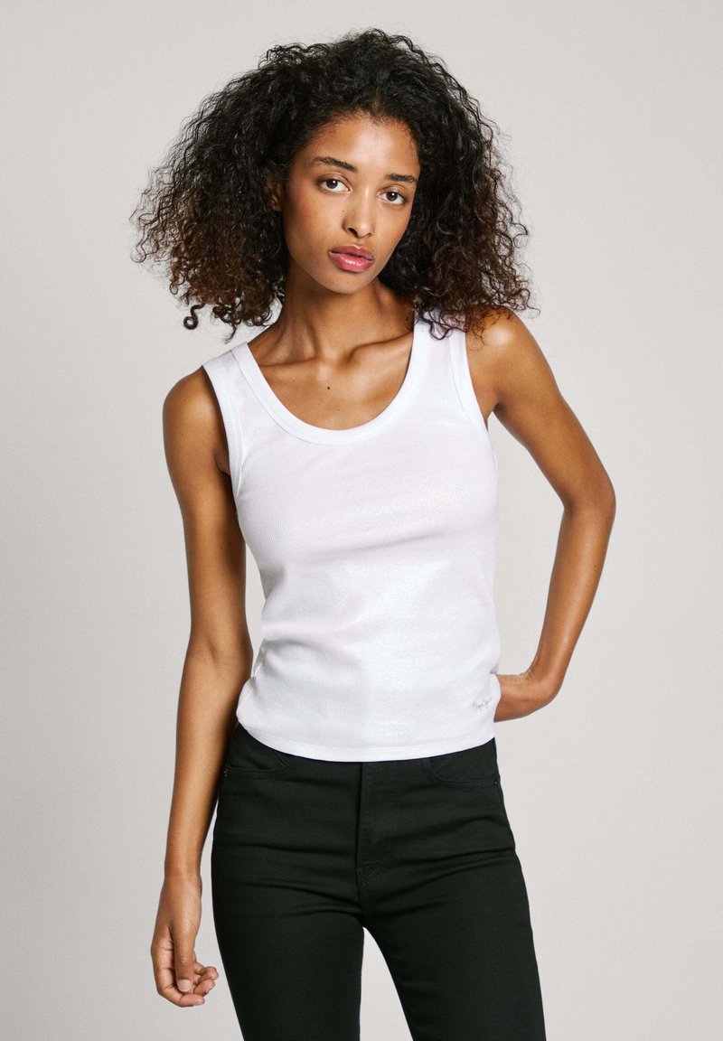 Top bianco senza maniche con scollo tondo, texture liscia e design aderente, abbinato a pantaloni neri. Look semplice e sobrio.