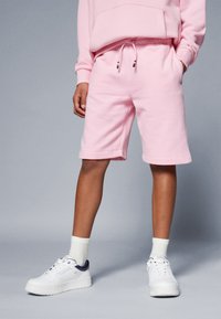 Rosa bomullsshorts med elastisk midja, sidofickor och uppvikta nederkanter. Kombinerat med vita sneakers och krämfärgade strumpor.