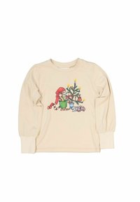 Krämfärgad långärmad skjorta med en färgglad illustration av en karaktär med rött hår bredvid en dekorerad julgran.