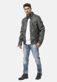 Schwarze Lederjacke mit gesteppter Verzierung, Frontreißverschluss, zwei Reißverschlusstaschen auf der Brust, getragen über einem weißen Hemd, kombiniert mit hellblauen Jeans und schwarzen Stiefeln.