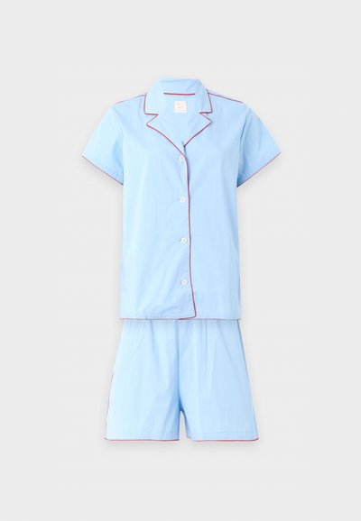 Haut de pyjama bleu clair à manches courtes avec boutons et col, ainsi que short assorti, tous deux avec un fin passepoil rouge le long des bords et des coutures.
