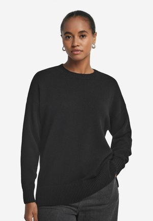 Schwarzer Strickpullover mit rundem Ausschnitt, gerippten Bündchen und Saum. Hat einen lockeren Schnitt und eine weiche Textur, kombiniert mit dunklen Jeans.