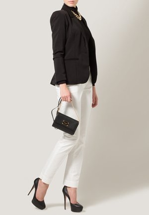 Schwarzer taillierter Blazer, weiße maßgeschneiderte Hose, schwarze High Heels und eine kleine schwarze Handtasche mit goldener Kettenriemen. Glatter Stoff und elegantes Design.