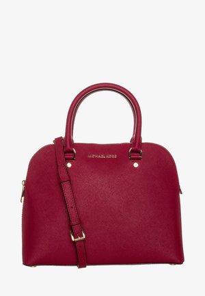 Rode Michael Kors handtas met afgeronde handvatten, verstelbare schouderriem en gouden accenten op een witte achtergrond.