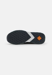 Svart gummisula på sneakers med mönstrat grepp, vit zigzagmönsterdetalj och orange logotyp vid hälen.