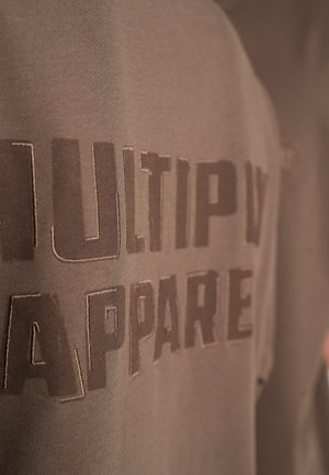 Brauner Baumwoll-Sweatshirt mit "MULTIPLY APPAREL" in großen Buchstaben bedruckt. Der Stoff hat eine glatte Textur und einen subtilen Glanz.