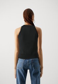 Svart ärmlös topp med ribbad fåll, figurnära design. Modellen bär blå hög midja jeans. Enkel och minimalistisk estetik.