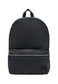 Mochila negra de nailon con forma redondeada en la parte superior, bolsillo frontal con cremallera y una etiqueta de tela en la parte inferior del frente. Cuenta con un asa superior para un transporte fácil.