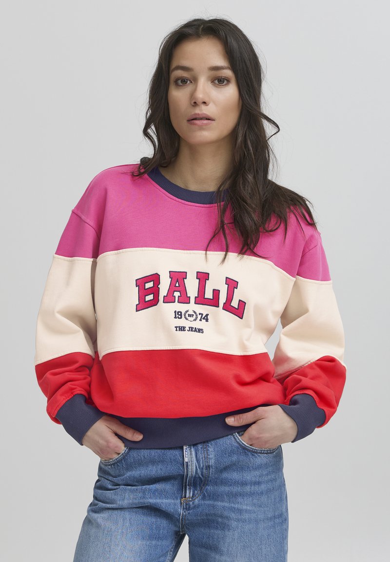 Dažādu krāsu jaopaka, kurai ir rozā, krējuma un sarkanās krāsas daļas ar tumši zilas krāsas joslu. Uz tās izceltā veidā ir rakstīts "BALL 1974 THE JEANS".