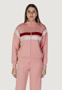 Tuta rosa con giacca zip-up caratterizzata da strisce orizzontali rosse e bianche. Tessuto morbido e vestibilità rilassata con pantaloni affusolati.