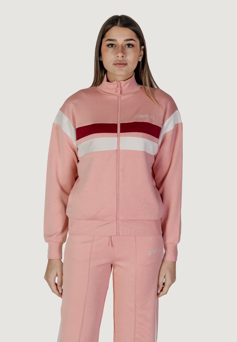 Tuta rosa con giacca zip-up caratterizzata da strisce orizzontali rosse e bianche. Tessuto morbido e vestibilità rilassata con pantaloni affusolati.