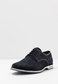 Chaussure en daim bleu marine foncé avec un bout arrondi, des coutures contrastantes et une semelle blanche avec un accent bleu. Dotée de lacets et d'une texture lisse.