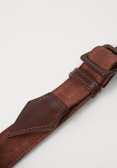 Ruda odinė apyrankė su lygiomis ir tekstūruotomis paviršiais, su rombo formos akcentu ir stačiakampiu sagtimi. Matomi patvarūs siūlai.