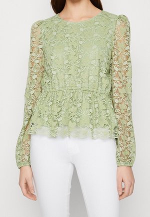 Top peplum in pizzo verde chiaro con maniche lunghe e trasparenti e motivo floreale. Presenta una vita arricciata e un colletto rotondo.
