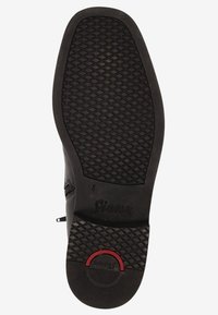 Semelle de chaussure noire avec un motif en diamant texturé, un accent rouge circulaire et le nom de marque gravé "Sioux" près du talon.