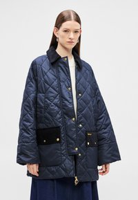 Tengerészkék steppelt dzseki fekete kordbársony gallérral, arany kapcsos gombokkal és két első zsebbel. Laza szabás, modellen bemutatva.