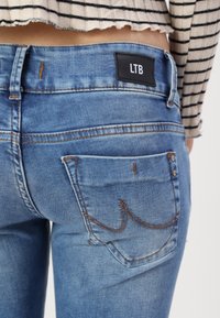 Jeans de mezclilla azul con una etiqueta negra de LTB en la parte trasera, costuras naranjas en contraste y un diseño clásico de bolsillo.