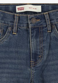 Gros plan sur la taille d’un jean bleu Levi's 511 Slim avec bouton, passants pour ceinture et étiquette de marque blanche.