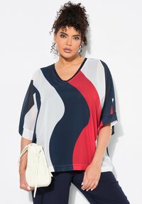 Top ampio con scollatura a V e audaci motivi ondulati in rosso, blu navy e bianco. Tessuto semi-trasparente con maniche larghe e dettagli in contrasto.