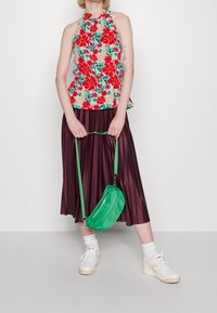 Květinový halter top s červeným a zeleným vzorem; plisovaná burgundská sukně; zelená crossbody taška; bílé tenisky se světle barevnými akcenty.