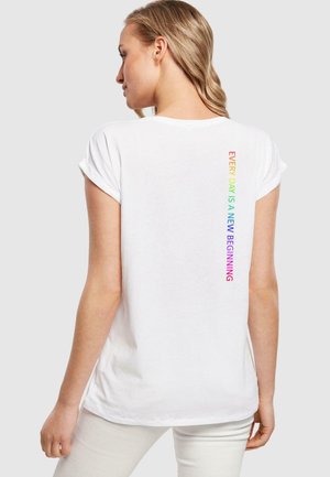 Weißes Baumwoll-T-Shirt mit aufgerollten Ärmeln und vertikalem Regenbogentext auf der Rückseite, der lautet: "JEDER TAG IST EIN NEUER BEGINN."