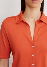Korte mouwen overhemd met knopen in een effen oranje stof. Voorzien van een kraag, vijf knopen en een gladde textuur. Geschikt voor casual draag.