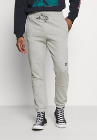 Pantaloni da tuta grigi realizzati in tessuto misto cotone, con cuciture laterali, polsini a costine e una piccola etichetta del marchio sulla coscia.