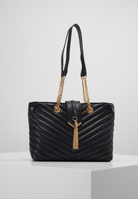 Mustan tikatun käsilaukun kultasävytteiset ketjut ja kahva, jossa on ristikkäin kiinnitettävä tupsu ja magneettiklipsi. Rakenne on nahkaa.