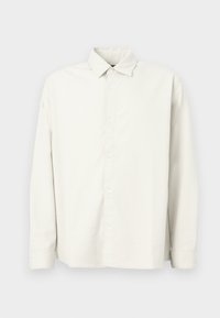 Chemise à manches longues beige clair à boutons, fabriquée dans un tissu texturé, avec un col standard, des rayures verticales et un ourlet droit.