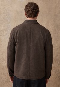Brown wool blend jacket with a collar, flat shoulders, and straight cut. Textured fabric and single button cuff accents.