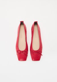Ballerines matelassées rouges avec un bout carré, présentant un accent en nœud et une doublure intérieure lisse. Le matériau semble brillant et texturé.