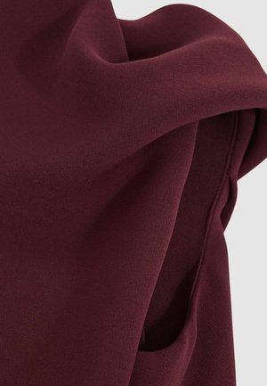 Burgundi színű, sima textúrájú anyag, amely lágyan lebeg. Finom varrással ellátott szélekkel és lágy, hullámos megjelenéssel rendelkezik.